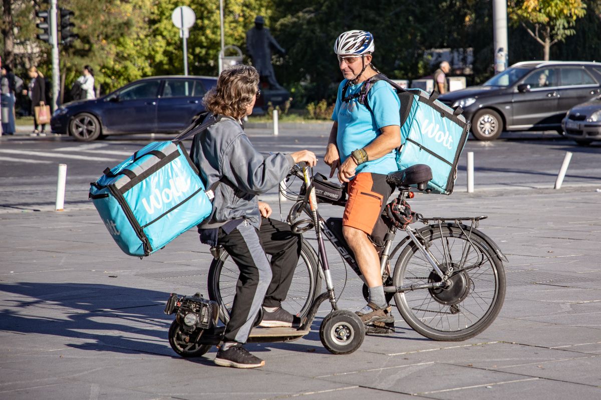 Deux coursiers avec de grands sacs de livraison discutent dans une rue en ville.