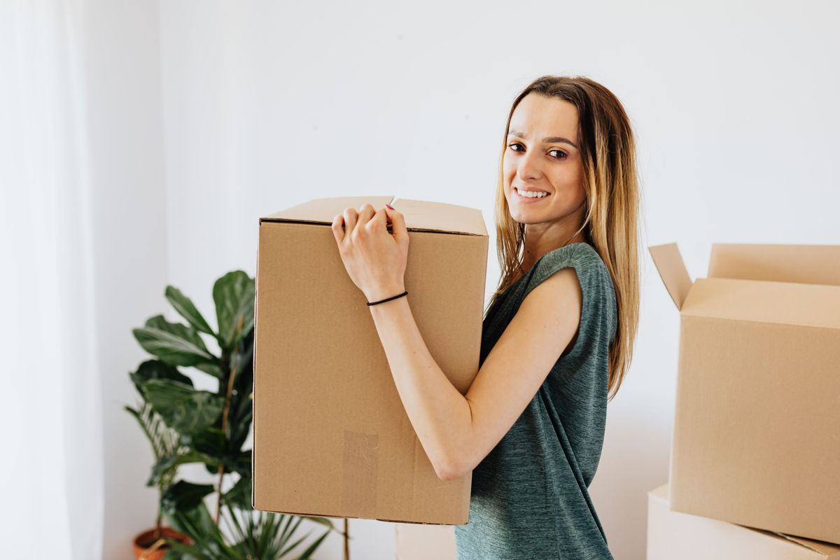 Une jeune femme sourit en portant un carton de déménagement.
