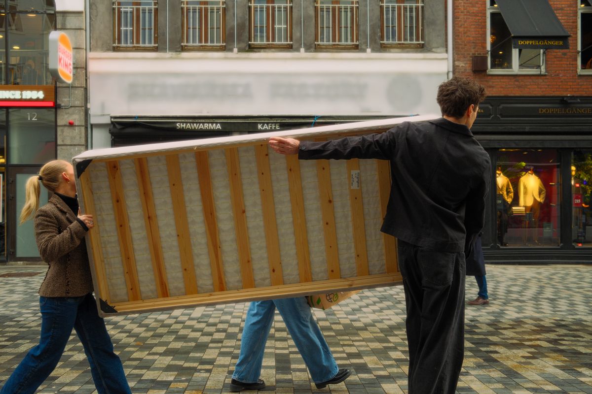 Deux personnes transportent ensemble un matelas dans une rue.